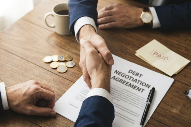 Aperto de maos sobre contrato de negociacao de divida ao lado de moedas e comprovante marcado como quitado
